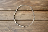a necklace with silver beads and a chain on a wooden table