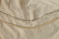 three gold chain necklaces laying on a beige cloth